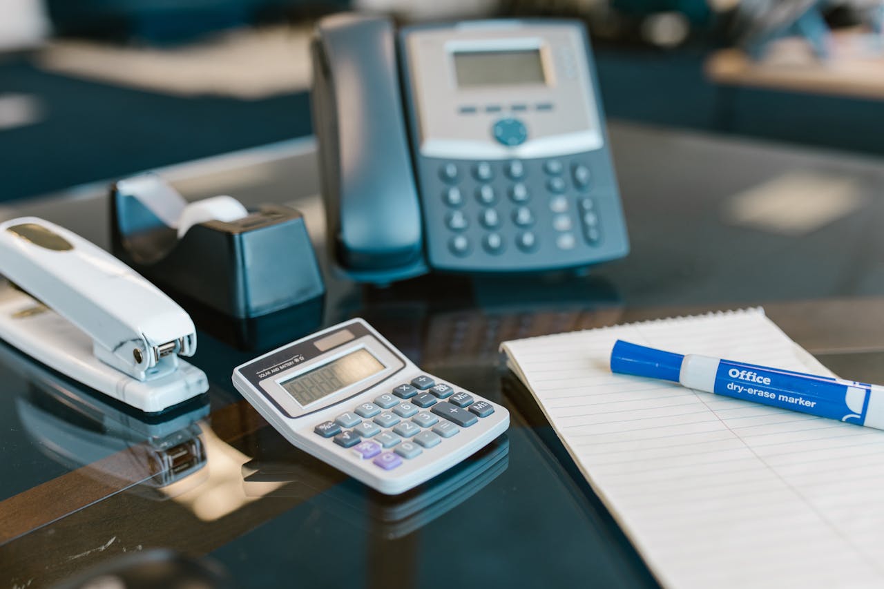 A modern office desk setup featuring various essential supplies including a calculator, stapler, and telephone.
