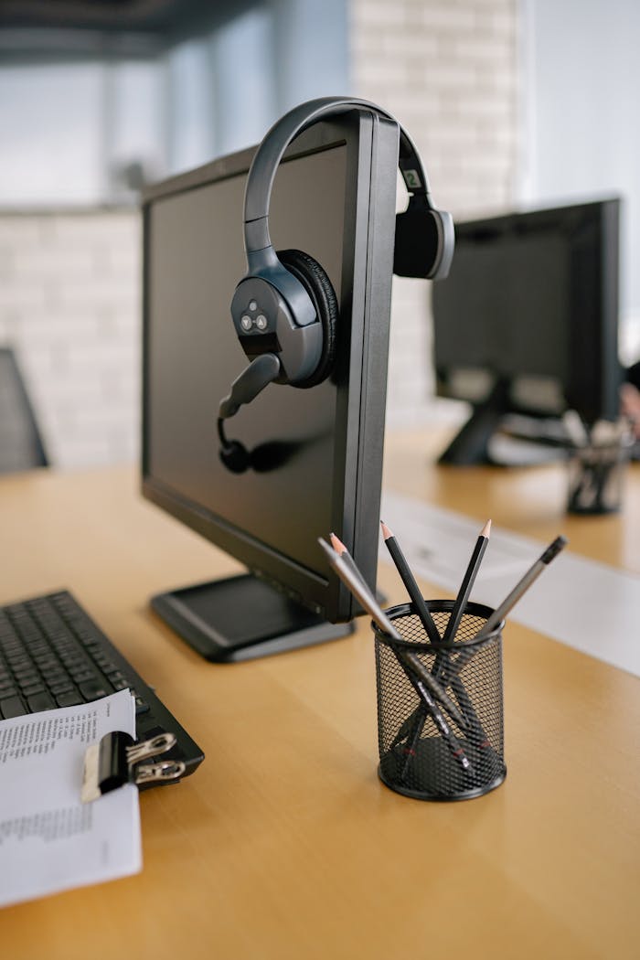 A sleek office setup featuring a monitor, headphones, and desk accessories on a wooden table.
